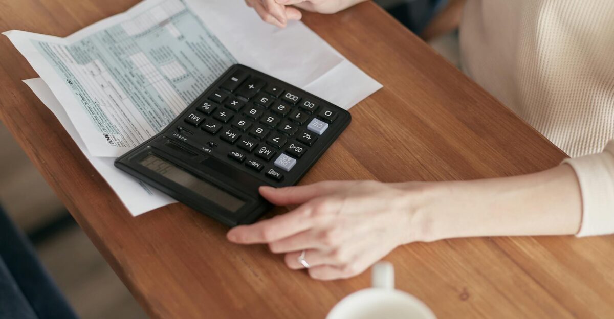 Focused individual using calculator to manage personal finances at wooden desk