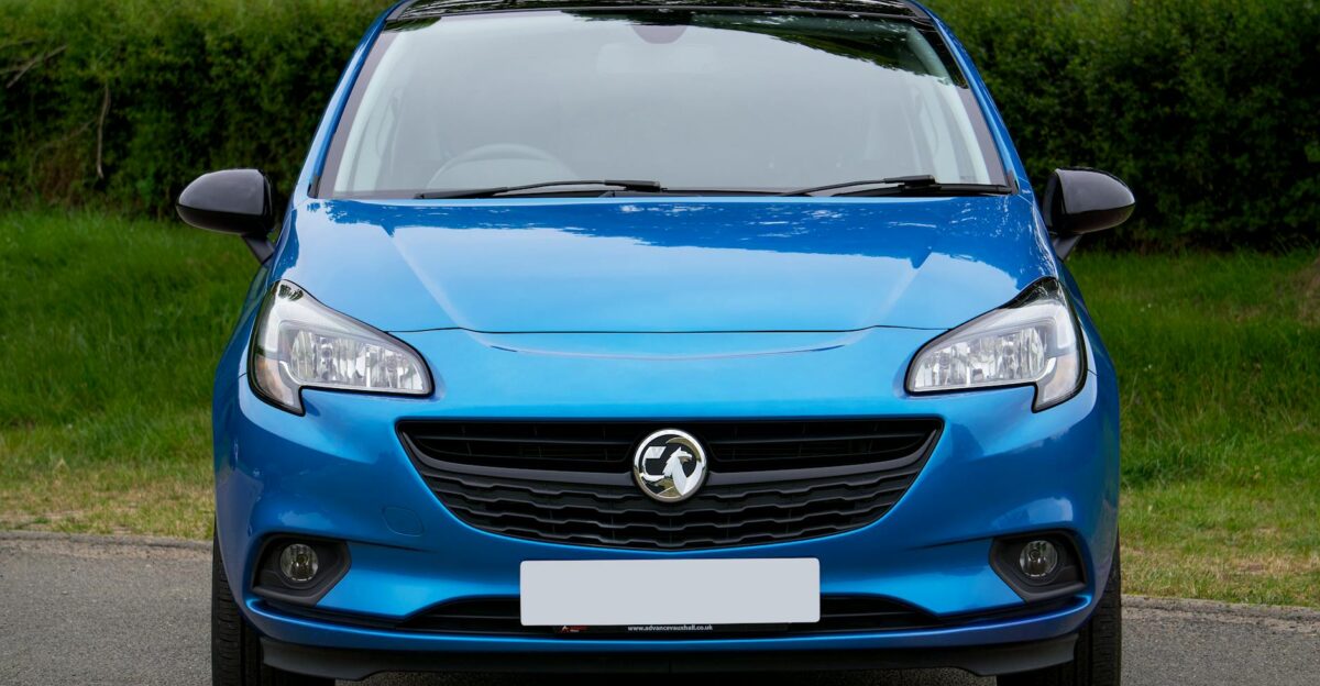 Front view of a blue Vauxhall Corsa car parked on a road with greenery in the background