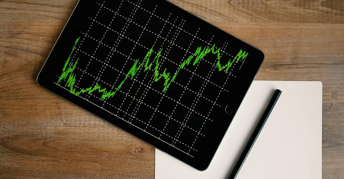 Flatlay of an iPad displaying stock market graph on a wooden desk with a pencil and paper