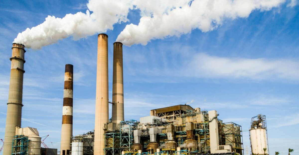 A large industrial power plant with smokestacks emitting smoke under a blue sky symbolizing pollution